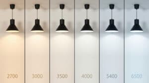 Six lampes suspendues identiques sont suspendues en rangée, chacune éclairant le mur avec des températures de couleur différentes - du jaune chaud au bleu froid - idéales pour rénover l'éclairage dans les bureaux et les commerces ou pour les projets Relamping LED.